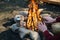 Outdoor horizontal image of traveler warming his hands by the campfire an in summer time.