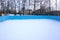 An outdoor ice skating rink and a hockey net with tall frost covered trees in the background in a winter landscape