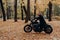 Outdoor image of male motorcyclist poses on fast motorbike, wears shades, black coat, enjoys ride in autumn park, breathes fresh
