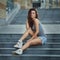 Outdoor lifestyle portrait of pretty young girl posing on stairway, wearing in hipster urban style on urban background