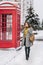 Outdoor photo of caucasian female model in gray coat and dark pants chilling in park with red call-box. Charming