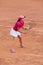 Outdoor photo of focused woman playing tennis on the court, dressed in pink t-shirt, cap and white skirt. Side view