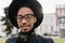 Outdoor photo of smiling african young man in big hat posing on blur city background. Close-up portrait of chilling guy