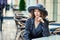 Outdoor photo of stylish woman wearing old fashioned coat, having break in street outdoor cafe