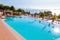 Outdoor pool with vibrant crystal water, parasols and deck chairs located on the coast of Garda with lake, hills and sun on