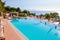 Outdoor pool with vibrant crystal water, parasols and deck chairs located on the coast of Garda with lake, hills and sun on