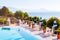 Outdoor pool with vibrant crystal water, parasols and deck chairs located on the coast of Garda with lake, hills and sun on