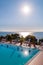 Outdoor pool with vibrant crystal water, parasols and deck chairs located on the coast of Garda with lake, hills and sun on