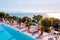 Outdoor pool with vibrant crystal water, parasols and deck chairs located on the coast of Garda with lake, hills and sun on