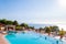 Outdoor pool with vibrant crystal water, parasols and deck chairs located on the coast of Garda with lake, hills and sun on