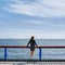 Outdoor portrait from back slim girl in a dress and denim jacket looking at sea