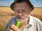 Outdoor portrait of bearded senior farmer ready to eat organic cucumber
