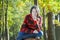 Outdoor portrait of cheerful young woman sitting on sawn tree trunk