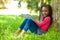 Outdoor portrait of a cute young black little girl reading a boo