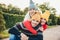 Outdoor portrait of handsome man give piggyback to his wife and daughter, wear warm clothes, have happy expressions, support each