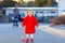 Outdoor portrait of little cute toddler girl in red coat aon spring sunny day with push wooden toy. Healthy happy baby