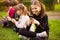 Outdoor portrait of positive inspired child, girl sitting on grass with legs crossed and using mobile phone in company