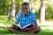 Outdoor portrait of student black boy reading a book