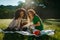 Outdoor portrait of two multi-ethnic girl friends spending time together on picnic on the sunny meadow. The young