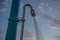 Outdoor Public Sprinkle for Swimmers under Cloudy Blue Sky. Angle Closeup View of Pipe Tied to Post by Plastic Strip