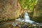 Outdoor scene featuring a lush waterfall cascading down a rocky wall