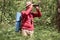 Outdoor shiot of man looking through binoculars in forest, senior traveller wearing casual clothing having adventure in wood,