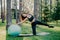 Outdoor shot of active brunette woman in sportswear poses on yoga mat, does stretching exercises with gymnsatic ball, poses in