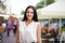 Outdoor shot of attractive brunette young female in white blouse, has stroll in city during summer day, poses at camera with pleas