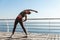 Outdoor shot of attractive and fit sportswoman workout on a pier. Girl stretching and training alone at the seaside