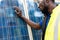 Outdoor shot of black African engineer inspect electrical solar panel wearing hardhat , protective eyeglass and safety equipment