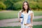 Outdoor shot of brunette woman dressed in casual t shirt, white trousers, keeps hand in pocket, drinks aromatic coffee during morn