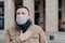 Outdoor shot of ill man wears medical mask against viruses, has shortness of breath and coughs, feels unwell, protects from