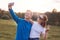 Outdoor shot of joyful teenagers embrace and stand next to each other against nature background, make selfie with modern smart pho