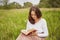 Outdoor shot of serious lovely young woman enjoys summer weather, sits on green field, reads interesting book with great interest,