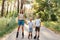 Outdoor shot of smiling attractive female with her little sons standing on road in summer park and holding hands, family