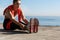 Outdoor shot of smiling confident sportswoman workout near sea. Fitness woman sitting on wooden pier and stretching legs