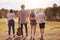 Outdoor shot of teenagers stand backs to camera, have walk on field, recreat during summer holidays, use guitar for singing songs,