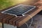 Outdoor shot of wooden bench in park having solar power panel installed, USB cabel connected to smartphone, modern device lying