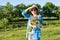 Outdoor summer portrait of an adult woman with bouquet of wildflowers, straw hat and sunglasses. Nature background, rural landscap