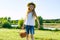 Outdoor summer portrait of little girl with basket strawberries, straw hat. Nature background, rural landscape, green meadow, coun