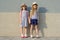 Outdoor summer portrait of two happy girl friends 7, 8 years holding hands. Girls in striped dresses, hats with backpack,