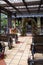 Outdoor tent made of wood, a wedding arch of green branches and red flowers, wooden benches on decorative wheels