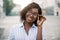 Outdoor urban close up portrait of stylish positive African woman in striped casual shirt, touching her eye glasses