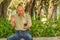 Outdoor view of old man sits on bench and saying hello on video cam with cellphone in his hand, enjoying the nature and
