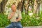 Outdoor view of old man sits on bench and saying hello on video cam with cellphone in his hand, enjoying the nature and