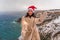 Outdoor winter portrait of elegant happy smiling woman in santa hat, light faux fur coat holding sparkler, posing