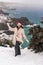 Outdoor winter portrait of happy smiling woman, light faux fur coat holding heart sparkler, posing against sea and snow