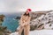 Outdoor winter portrait of happy smiling woman, light faux fur coat holding heart sparkler, posing against sea and snow