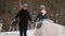 Outdoor winter shot of young wedding couple running and having fun holding hands in snow weather pine forest during