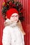 Outdoor winter young blonde teen girl portrait. Christmas wreath and red painted wooden door at background.